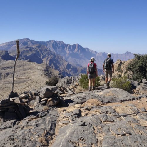 Un escursionista cammina lungo il sentiero in cresta di Sharaf Al Alamayn con vista panoramica sulle montagne e i canyon dell'Oman.