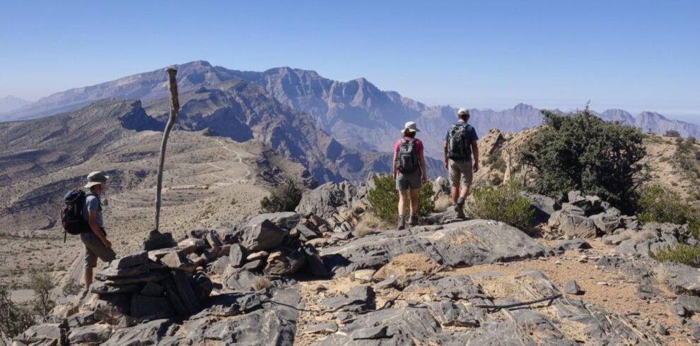 Un escursionista cammina lungo il sentiero in cresta di Sharaf Al Alamayn con vista panoramica sulle montagne e i canyon dell'Oman.