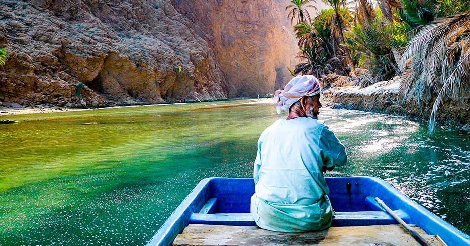Un uomo su una piccola imbarcazione attraversa le acque turchesi all'ingresso del canyon di Wadi Shab, Oman.