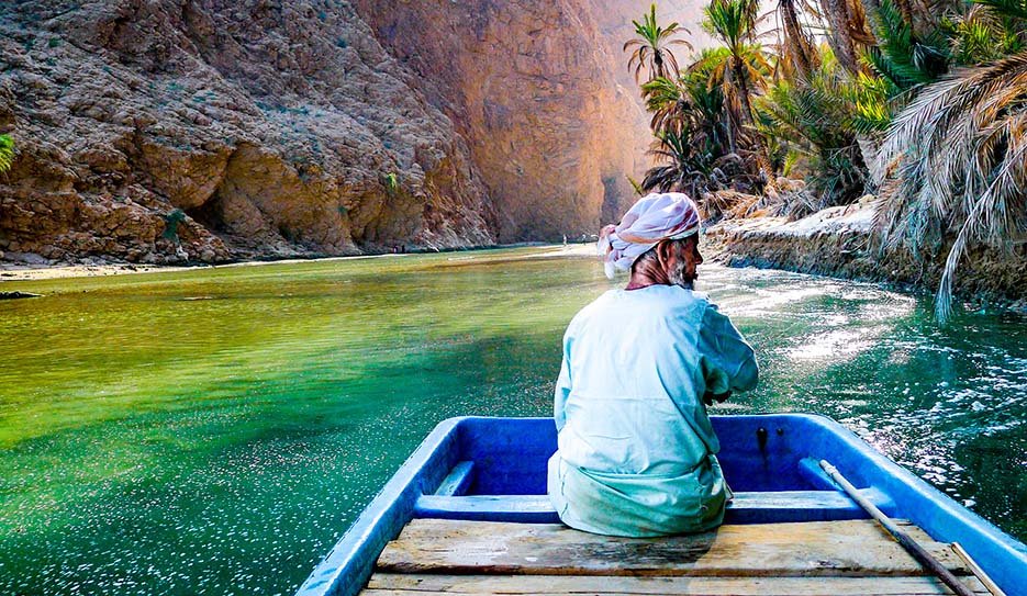 Un uomo su una piccola imbarcazione attraversa le acque turchesi all'ingresso del canyon di Wadi Shab, Oman.