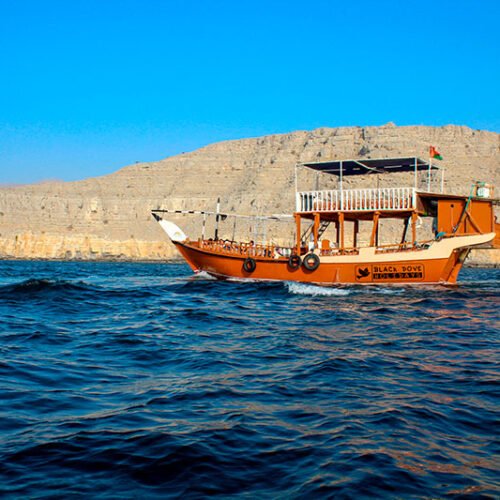 Een traditionele houten dhow vaart door de diepblauwe fjorden van Musandam omringd door kalksteenrotsen