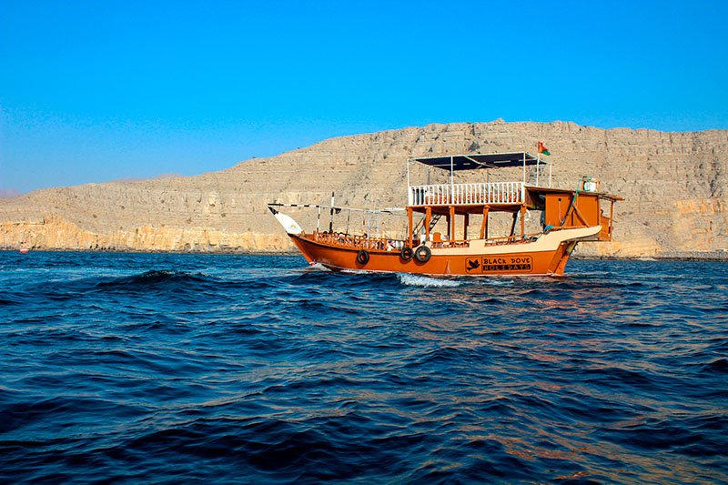 Een traditionele houten dhow vaart door de diepblauwe fjorden van Musandam omringd door kalksteenrotsen